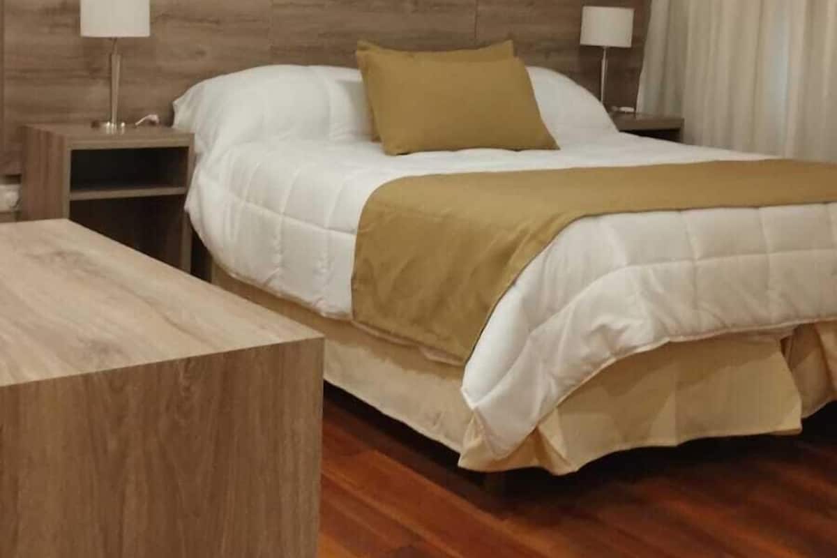 A bedroom with a wooden headboard, a bed with white and beige bedding, two bedside tables with lamps, and a hanging light fixture.