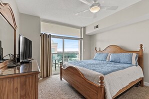 Un dormitorio con una cama grande, televisión, cómoda de madera y balcón con vistas.