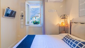 Un dormitorio con cama, televisor, aire acondicionado, ventana con vistas a edificios y un pez decorativo en la pared.