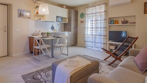 Un espacio habitable compacto con kitchenette, zona de comedor, sala de estar con sofá y sillón, y televisor.