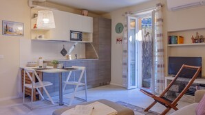 Un espacio habitable compacto con kitchenette, comedor, zona de estar con sofá y sillón, y televisor.