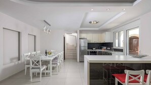 Una cocina moderna con armarios blancos, una isla central y una zona de comedor con sillas y mesa blancos.
