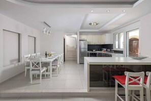 Una cocina moderna con armarios blancos, una isla central y una zona de comedor con sillas y mesa blancos.