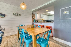 Zona pranzo con tavolo di legno e sedie blu, cucina sullo sfondo e termostato a parete.