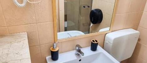 A small bathroom with a sink, toilet, and a mirror. There is a hairdryer on the wall and a towel rack.