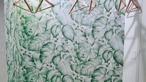 A bathroom with a green leaf pattern wallpaper, wooden hangers, a white towel, a woven basket, and a wooden crate. - Ecorooms (Ferrara)