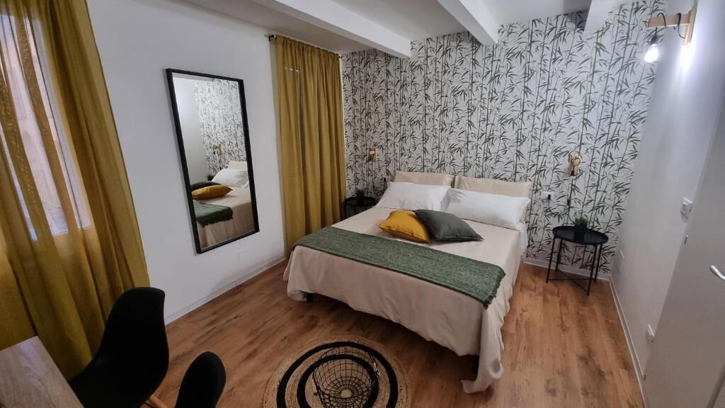 Ein Schlafzimmer mit einem Bett, einem Sessel, einem Spiegel und einem Nachttisch.
