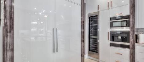 A modern kitchen with white cabinets, a built-in oven, and a coffee machine.