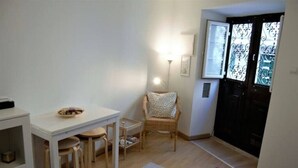 Une petite pièce accueillante, avec une table à manger, des chaises, un fauteuil en osier, une lampe blanche et une porte ornée de panneaux de verre décoratifs.