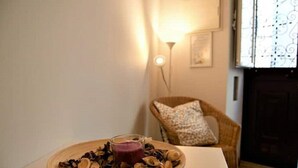 Une pièce comprenant une table en bois sur laquelle se trouve un bol de fruits secs et de noix, un verre d’une boisson violette et une chaise en osier avec un coussin.