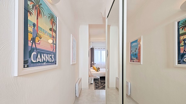 A hallway with framed posters, a bed with a view, and a tiled floor. - Viva Riviera Quiet Studio Carré d'Or (Cannes)
