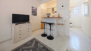 A modern kitchen with white cabinets, a built-in oven, and a microwave. There is a bar area with stools and a clock on the wall. - Viva Riviera Quiet Studio Carré d'Or (Cannes)