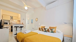 A hotel room with two beds, a kitchenette, a ceiling fan, and a nightstand with a lamp. - Viva Riviera Quiet Studio Carré d'Or (Cannes)