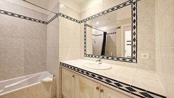 Un baño con bañera, lavamanos y un espejo grande.