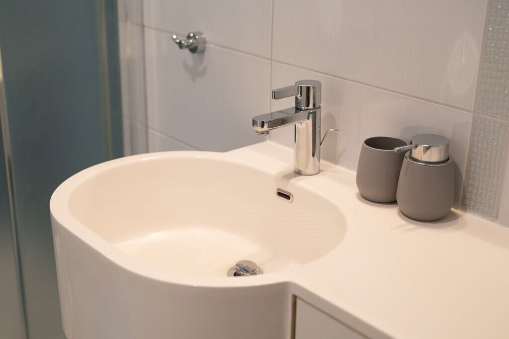A modern bathroom with a white sink, chrome faucet, and two gray cups on the countertop.