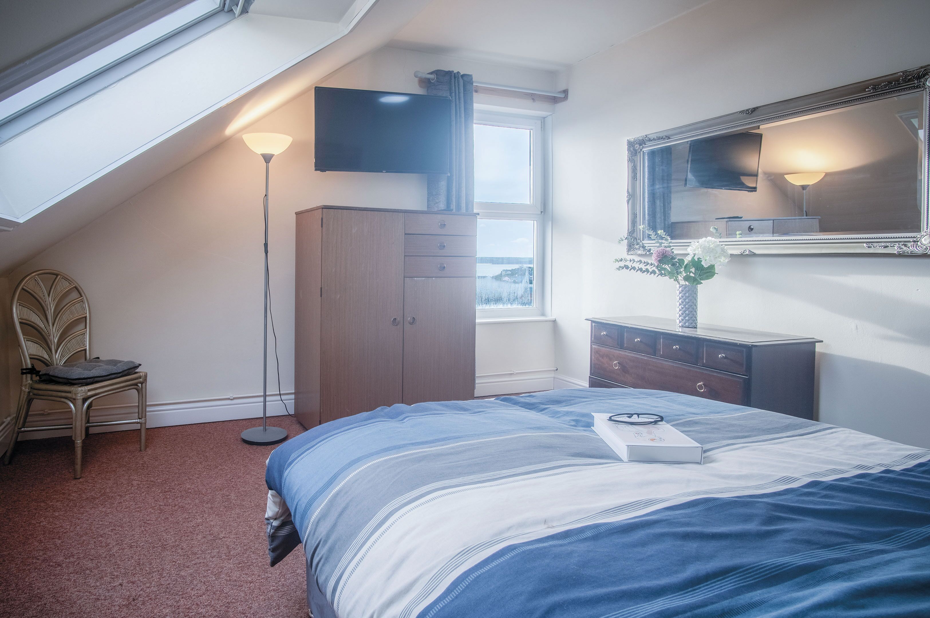 A bedroom with a bed, a dresser, a chair, a TV, and a window.