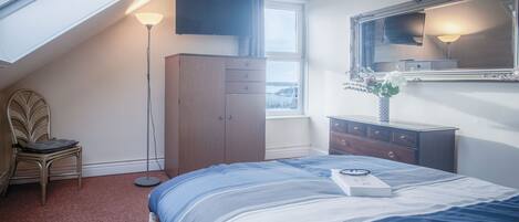 A bedroom with a bed, a dresser, a chair, a TV, and a window.