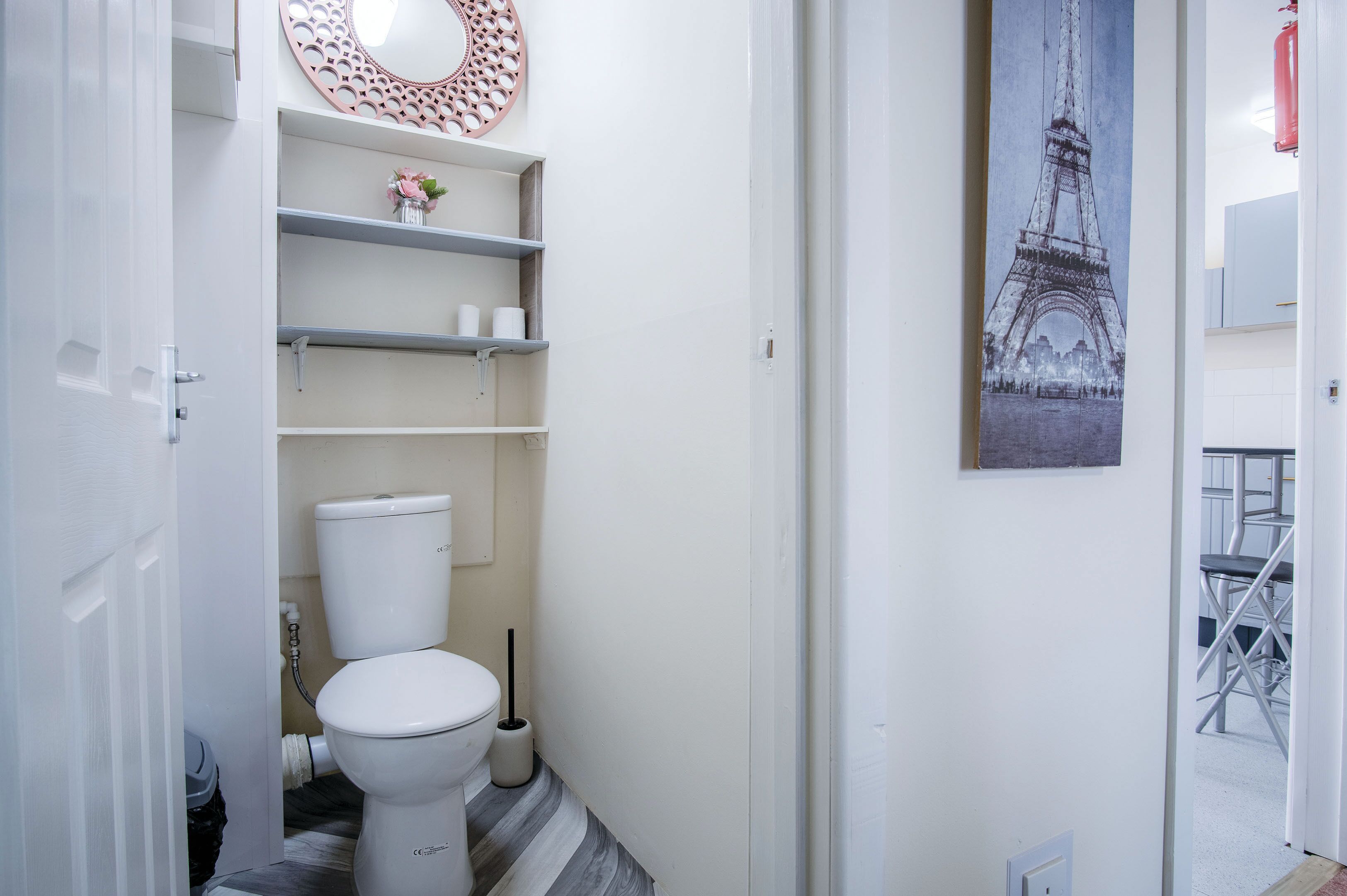 Un baño con inodoro, repisas, un espejo y un cuadro de la Torre Eiffel.