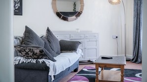 A modern living room with a grey sofa, a round mirror, a small wooden table, and a floor lamp. - Fulke Street - 2 Bedroom Apartment - Milford Haven (Milford Haven)