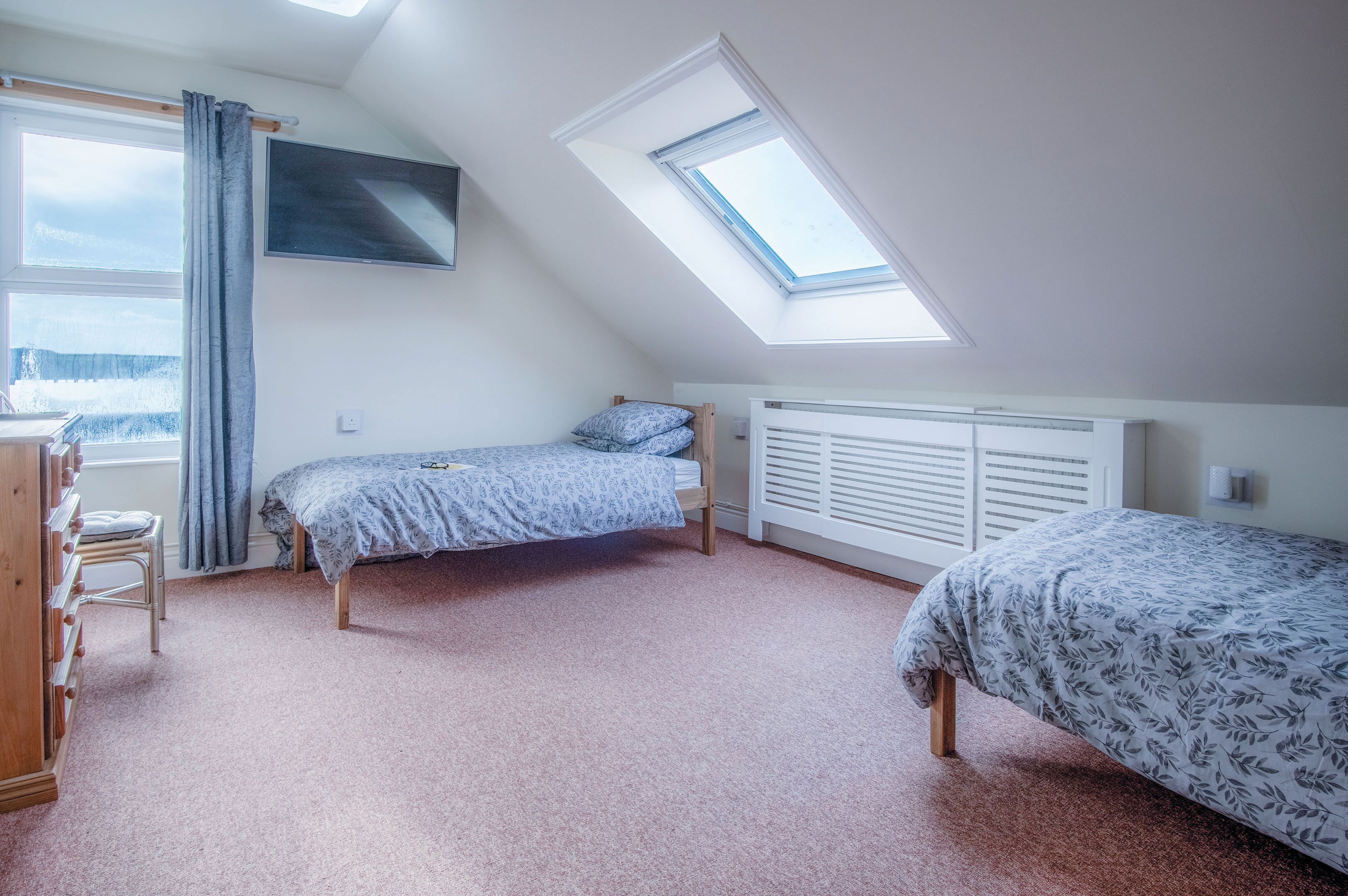Een slaapkamer met twee bedden, een raam, een radiator en een televisie aan de muur.