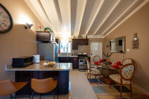 A modern kitchen with a central island, dark cabinetry, and a dining area with patterned chairs. - La Mansion Monet (St. Ann's Bay)