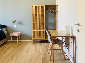 A room with a wooden floor, a bed with a dark headboard, a pink side table, a wooden wardrobe with a hanging rack, and a wooden dining table with chairs. - Casa Duci - Two Bedroom Apartment, Sleeps 4 (Rome)