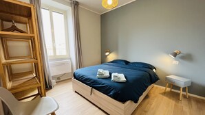 Ein modernes Schlafzimmer mit einem Bett, Nachttischlampen, einem Holzschrank, einem Sessel und einer Heizung.