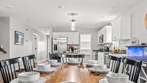 A modern kitchen with white cabinets, a central island, and a dining area with a wooden table set for six. - Bourbon Trail Near Buffalo Trace-Hot Tub, Fire Pit, BBQ Grill (Frankfort)