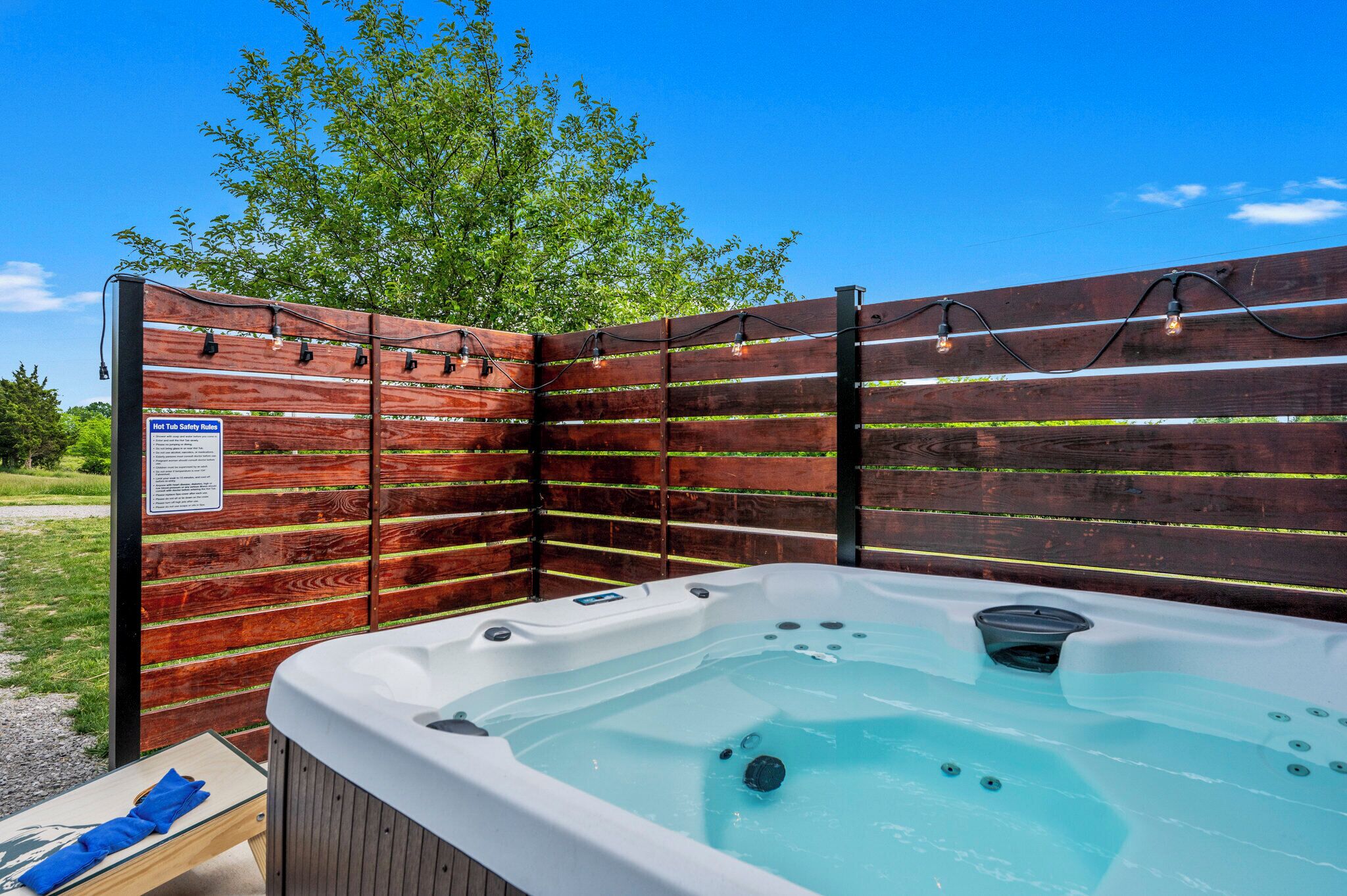 Ein Whirlpool mit Holzterrasse und Sicherheitshinweis, umgeben von einem Holenzaun und Lichterkette.