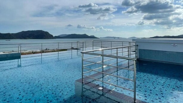 Une piscine à débordement dotée d’une structure en métal, offrant une vue dégagée sur une étendue d’eau et sur des montagnes lointaines, et surplombée d’un ciel partiellement nuageux.
