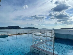 An infinity pool with a metal frame structure, a clear view of a body of water and distant mountains, and a partly cloudy sky. - Langkawi Homestay Family Suite (Langkawi)