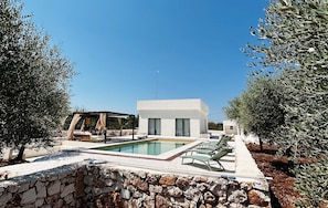 A modern villa with a swimming pool, outdoor seating, and olive trees.