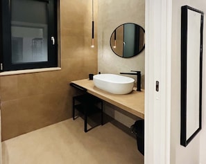 A modern bathroom with a large white sink, a round mirror, and a black chair.