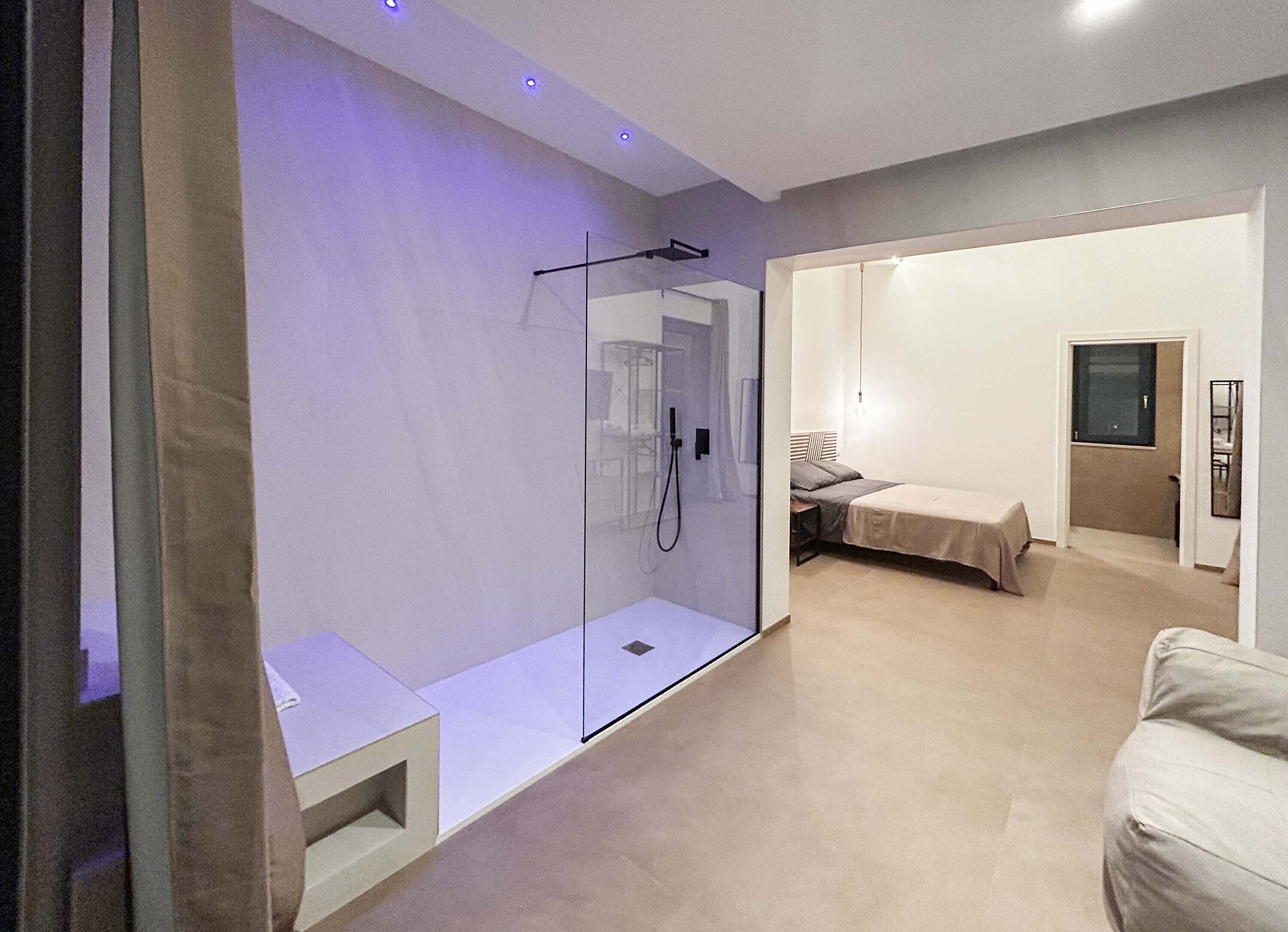 Ein modernes Schlafzimmer mit Glasdusche, einem Bett und einem kleinen Tisch.