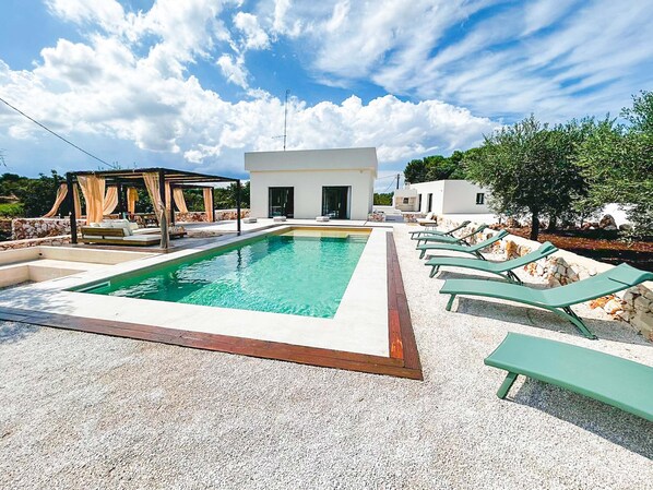 A modern outdoor pool area with a clear blue sky, a white building, and lounge chairs.