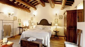 A bedroom with a large bed, wooden beams, wall-mounted lamps, and a wooden wardrobe. - Casatorre 6+2, Emma Villas (Saludecio)