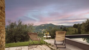 Two chairs facing a pool with a table between them, overlooking a scenic landscape with hills and a sunset sky. - Casatorre 6+2, Emma Villas (Saludecio)