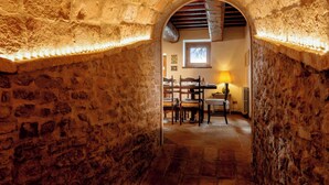 A stone-walled corridor leading to a dining area with a table and chairs, a window, and a lamp. - Casatorre 6+2, Emma Villas (Saludecio)