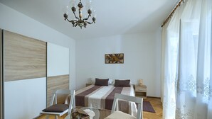 Une chambre à coucher moderne, avec un lit, deux tables de chevet, un lustre et une grande fenêtre ornée de rideaux légers.