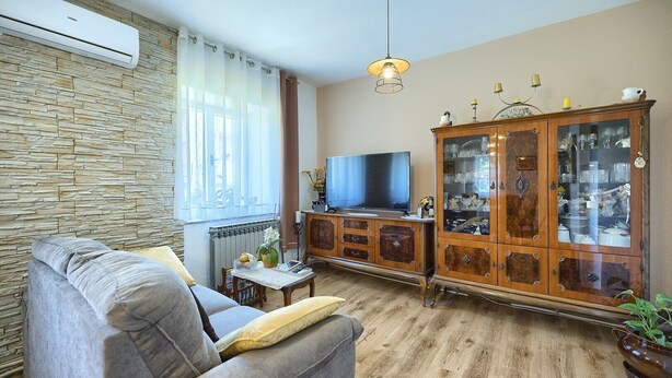 Un salon avec un mur en pierre, un canapé, un téléviseur, un meuble avec des portes en verre et un luminaire suspendu.