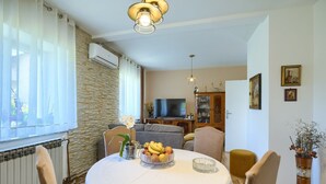 Un coin repas avec une table ronde, des chaises, un saladier de fruits et une plante en pot.