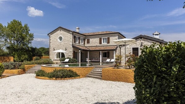 A stone villa with a swimming pool, outdoor seating, and a well-maintained garden.