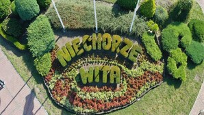 A circular garden with the words "NECHORZE WITA" in the center, surrounded by various types of shrubs and trees.