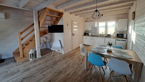 A modern kitchen with wooden beams, a dining area with blue chairs, and a staircase leading to another level.
