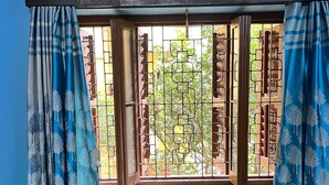 A room with a sofa, patterned cushions, a window with metal bars, and an air conditioning unit. - Home away from Home in a city with Garden View. 
Experience the magic yourself (Kolkata)