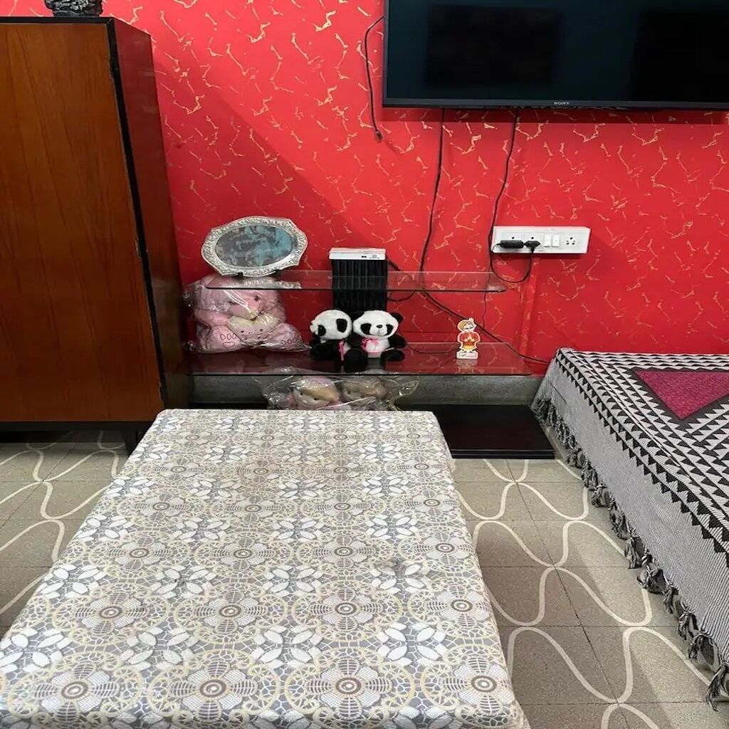 Habitació amb llit estampat, televisió penjada a la paret i una taula petita amb objectes decoratius.