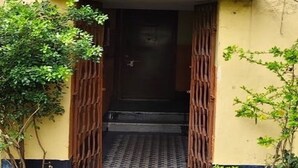A building entrance with a metal gate, a concrete path, and greenery on either side. - Home away from Home in a city with Garden View. 
Experience the magic yourself (Kolkata)