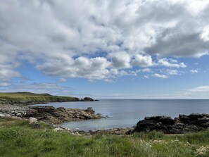 Un paysage côtier caractérisé par des rivages rocheux, des zones herbeuses et un ciel dégagé parsemé de nuages.