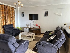 A living room with a sofa set, a coffee table, a TV, and a small cabinet. - Lux Suites Fox Hills Apartments Nanyuki (Nanyuki)
