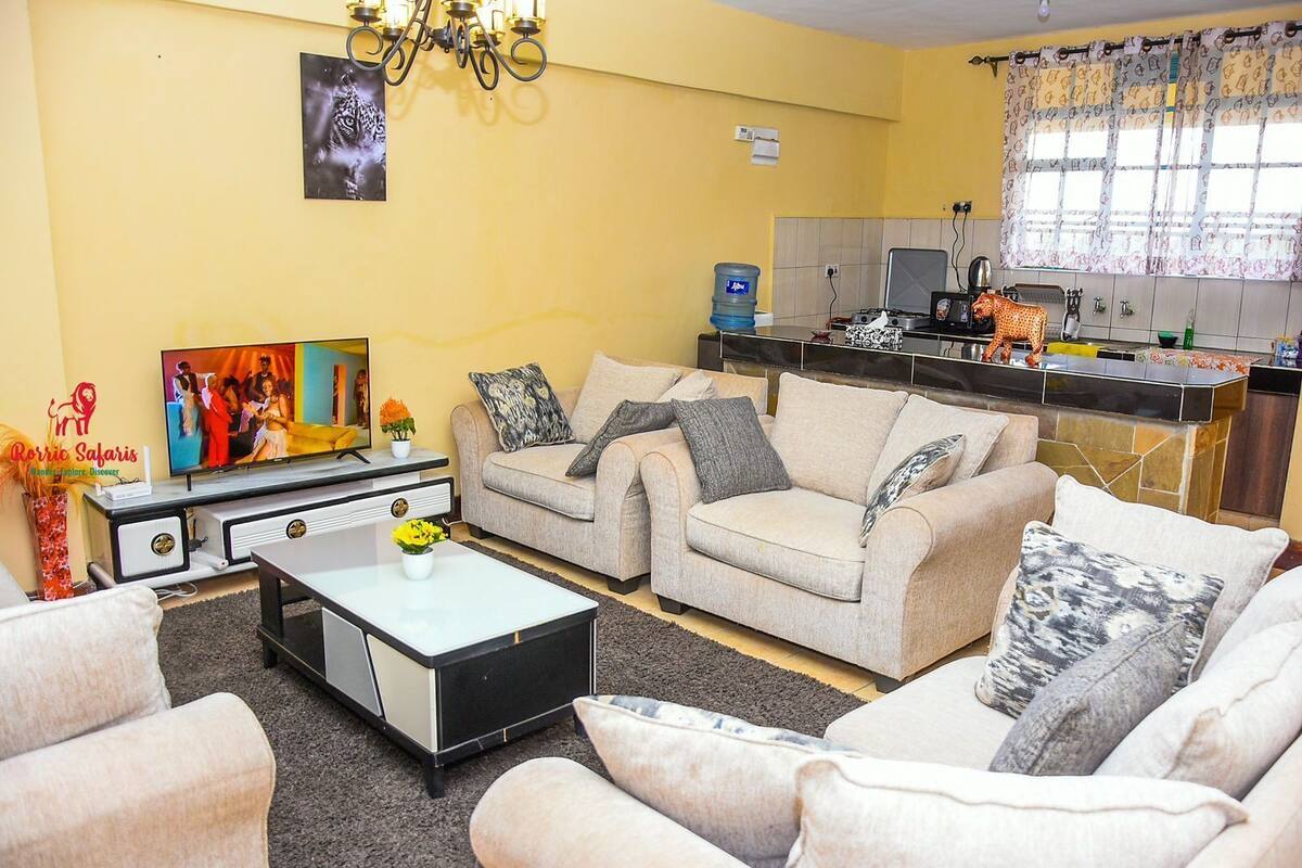 Ein Wohnzimmer mit einer Sofagarnitur, einem Couchtisch, einem Fernseher und einer Küchenzeile mit Herd und Spüle.